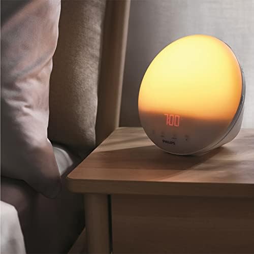 Le radio-réveil Philips SmartSleep en situation, posé sur une table de chevet à côté d'un lit. L'heure 7:00 est affichée.