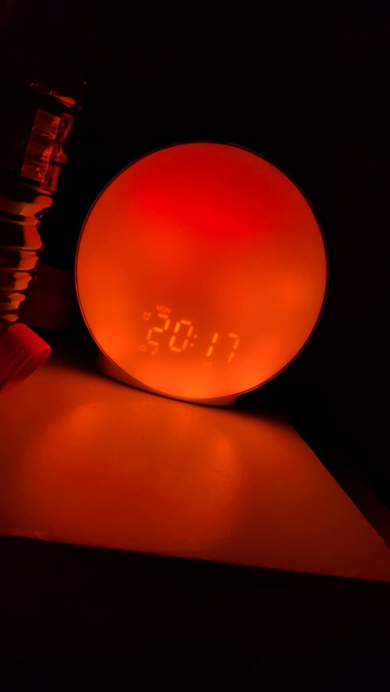 Le réveil est posé sur une table de chevet, allumé avec une lumière rouge-orangée et l'heure affichée.