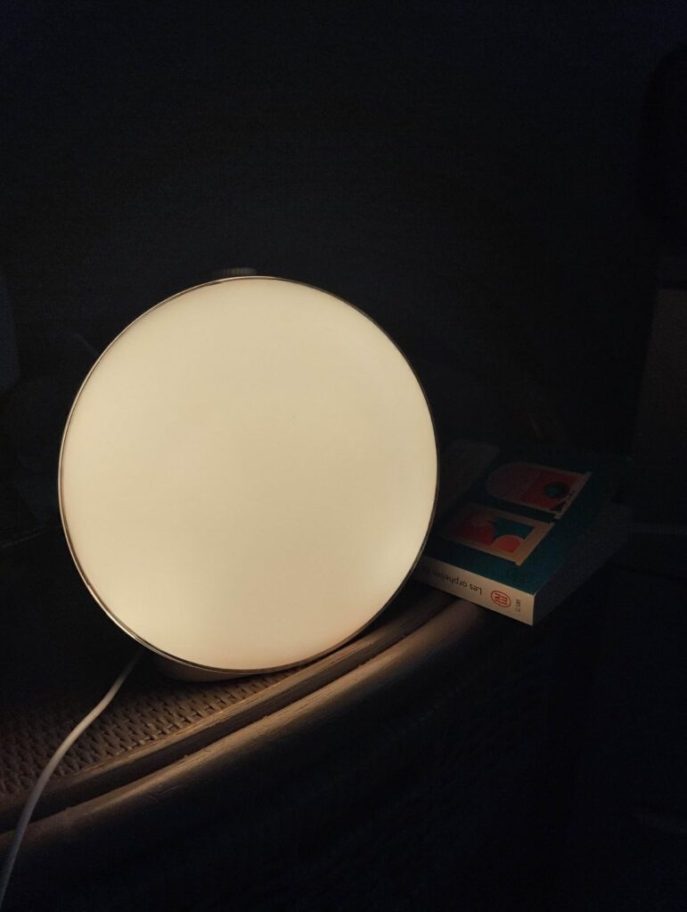 Le réveil est posé sur une table de chevet, allumé avec une lumière blanche.
