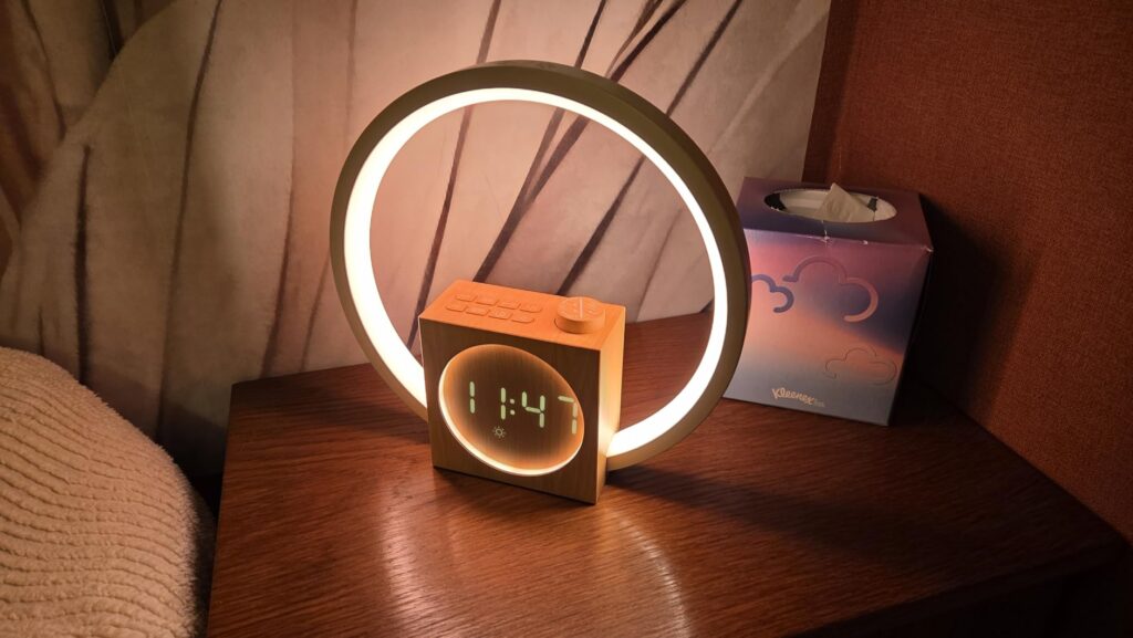 Le réveil-matin lumineux sur une table de chevet avec l'anneau allumé en blanc chaud et l'heure affichée.