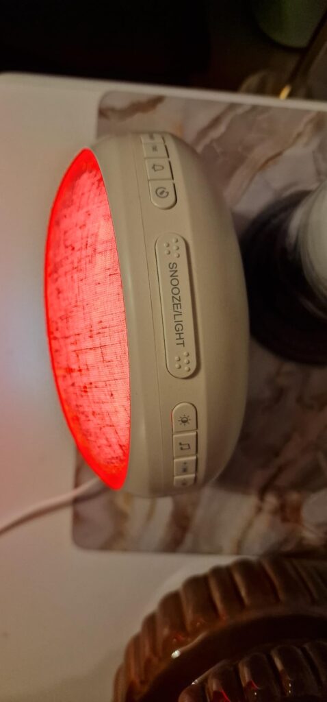 Vue latérale du réveil lumineux en fonctionnement avec lumière rouge, montrant les boutons sur le dessus.