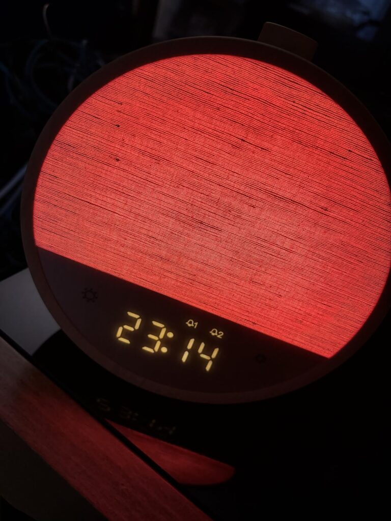 Vue de face du réveil dans l'obscurité. L'écran est rouge et affiche '23:14'.