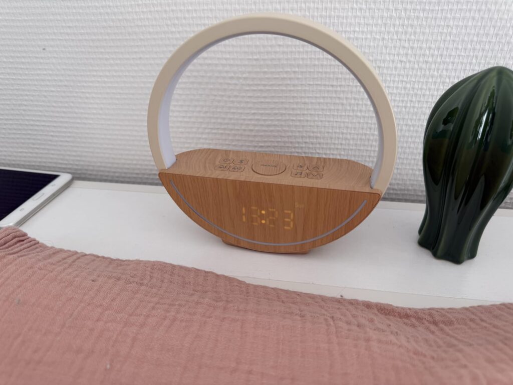 Le réveil-lampe est posé sur une table de chevet, non allumé. L'heure n'est pas visible. L'objet est montré sous un angle dif...