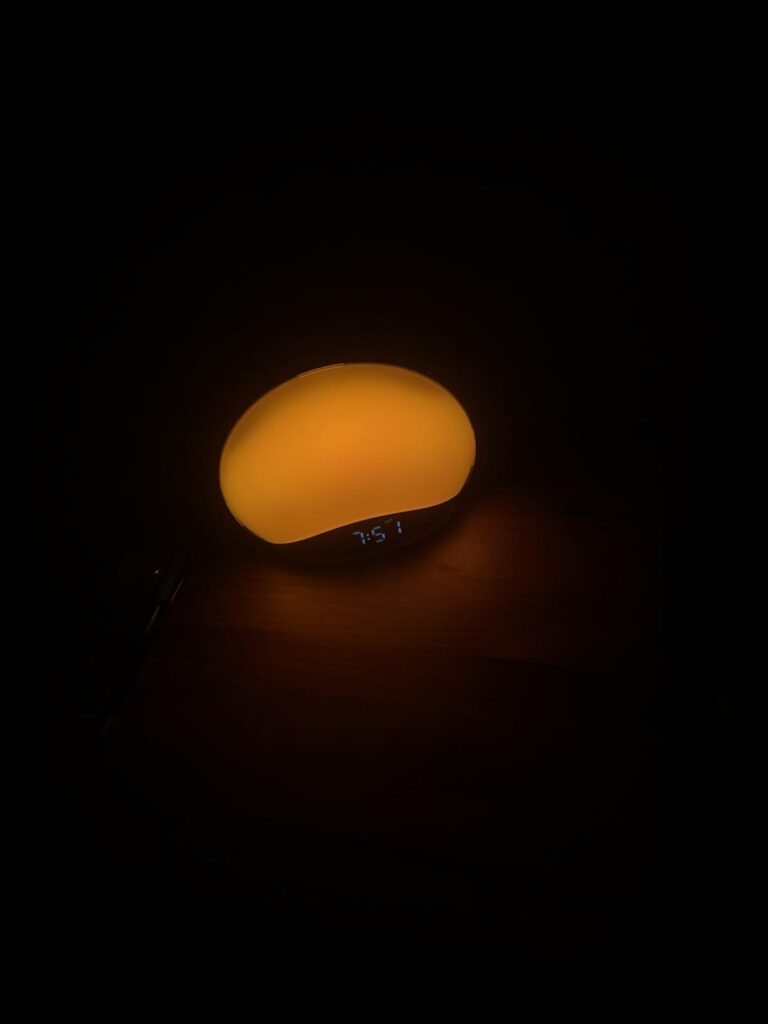 Le réveil lumière de face, allumé en lumière orange tamisée, sur un fond noir. Le bas du réveil est orange foncé et n'est pas...
