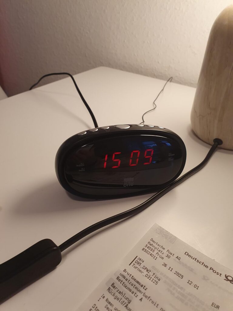 Radio-réveil posé sur une table de chevet avec une lampe et un reçu en dessous.
