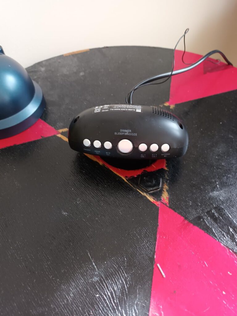 Vue du dessus du radio-réveil sur une table, montrant les boutons et l'arrière de l'appareil. Mêmes objets que le visuel 0.
