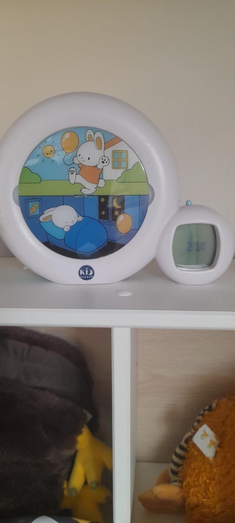 Réveil pour enfant posé sur une étagère, affichant une image de lapin endormi et une heure