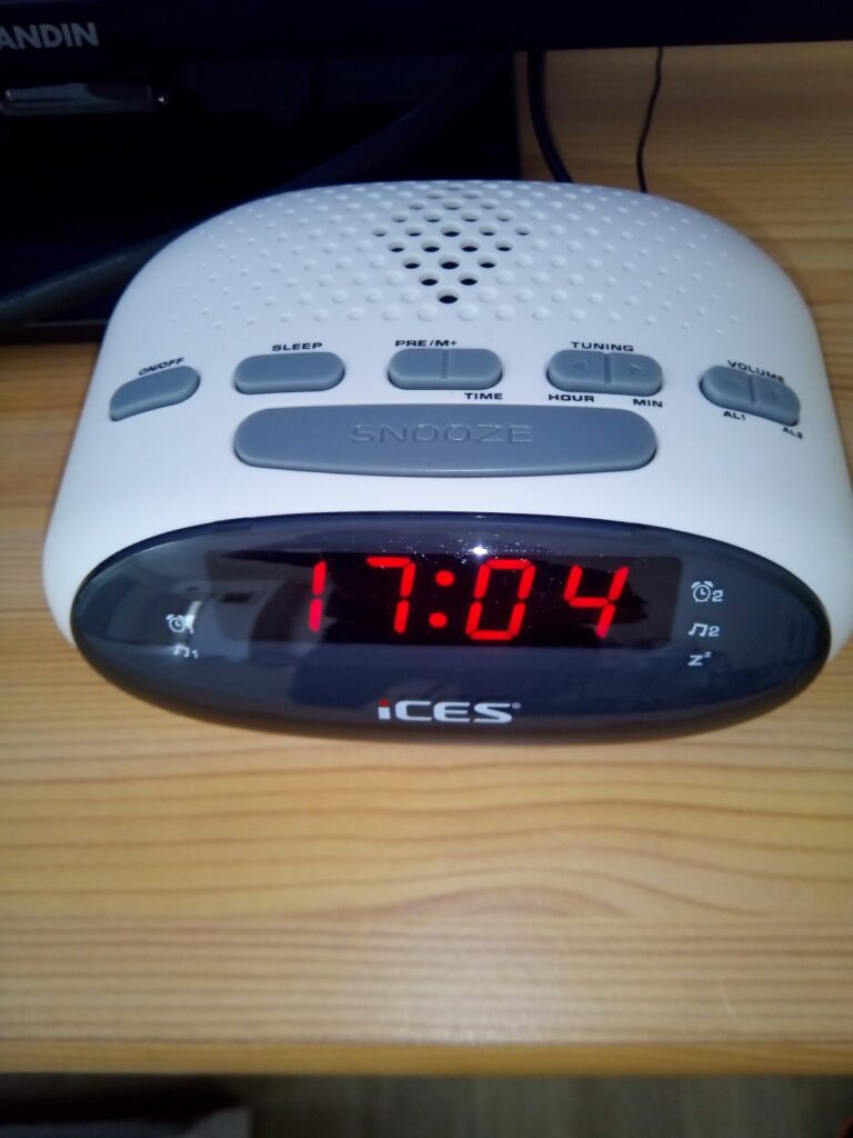 Radio-réveil blanc en situation sur une table en bois, affichant l'heure 17:04.
