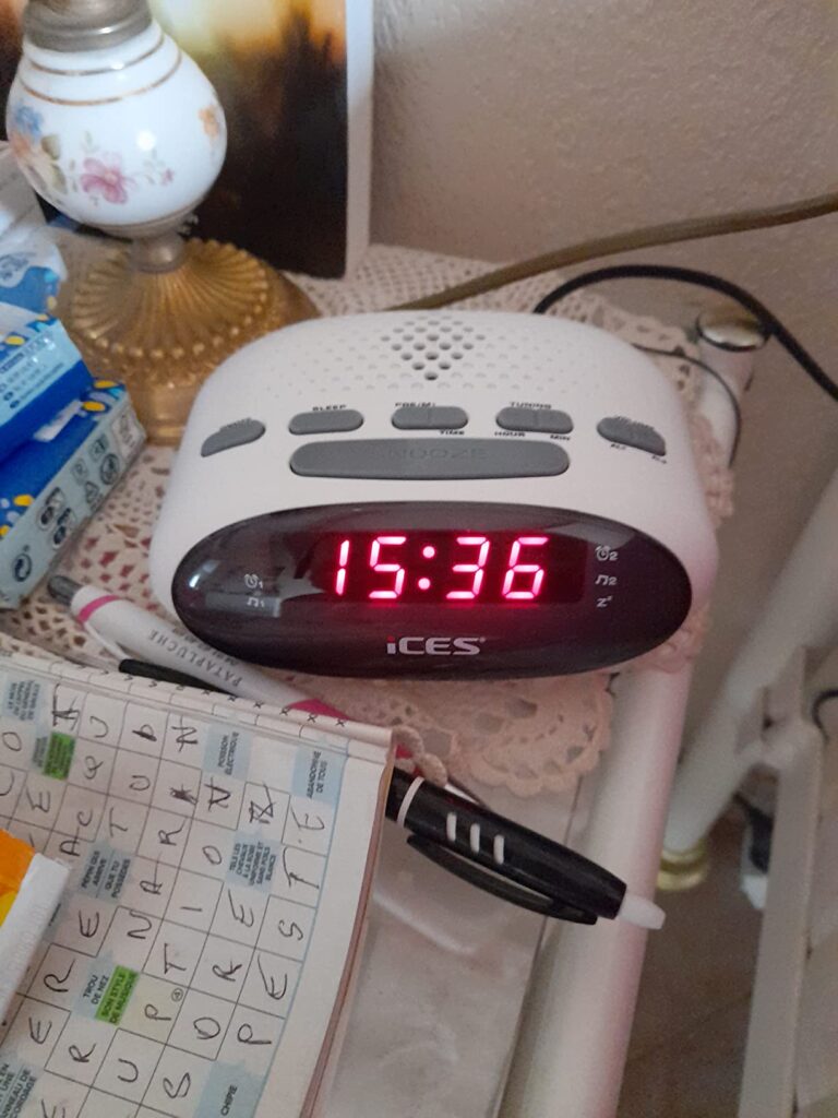 Radio-réveil blanc en situation sur une table de chevet, affichant l'heure 15:36.