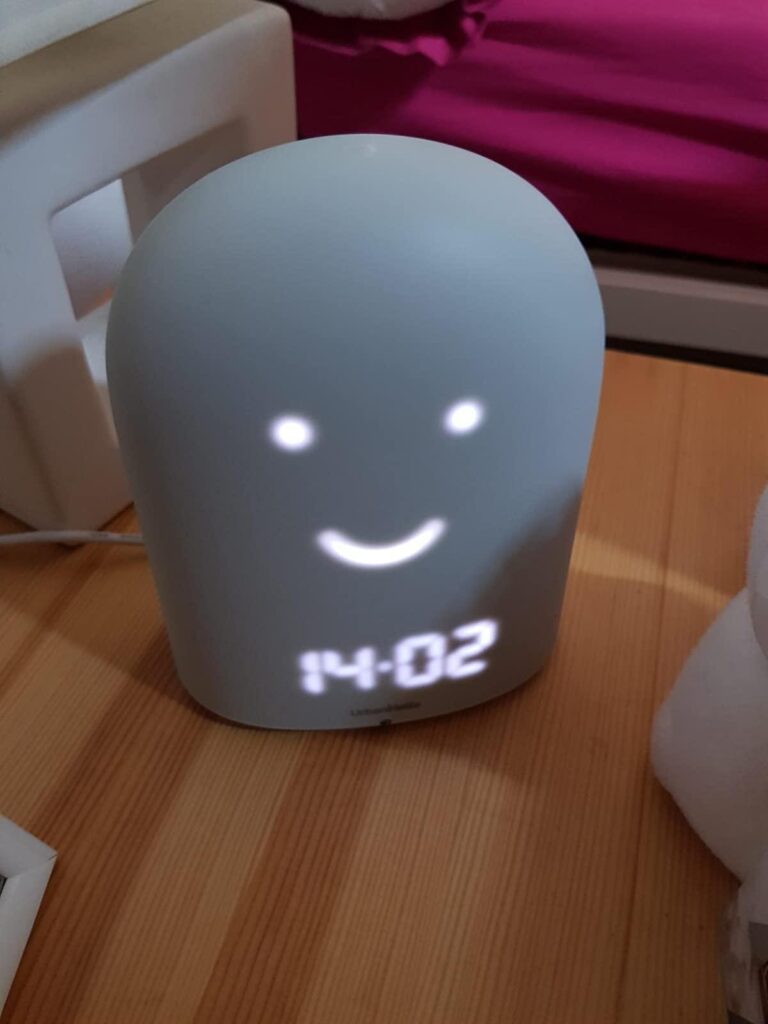 Le Remi est montré de face, dans une chambre d'enfant. L'écran affiche l'heure '14:02' et un visage souriant.