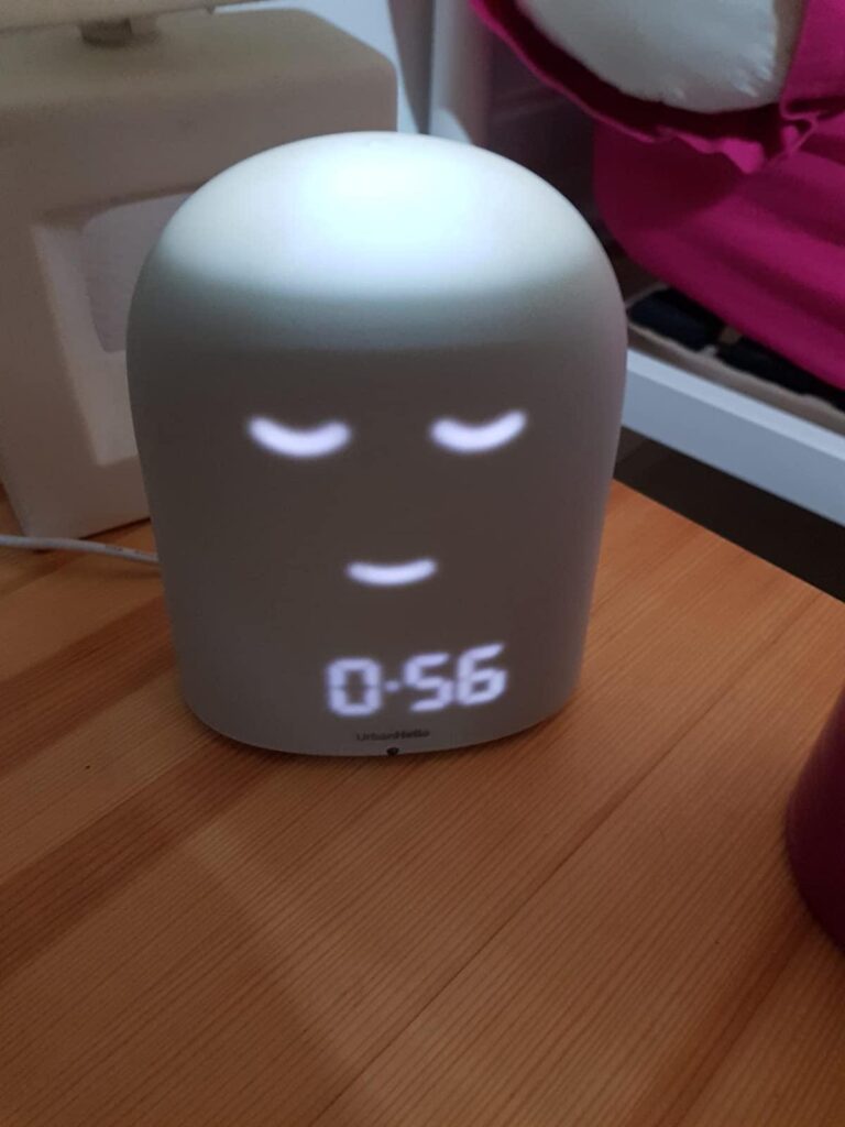 Le Remi est montré de face, dans une chambre d'enfant. L'écran affiche '0:56' et un visage endormi. L'image est légèrement di...