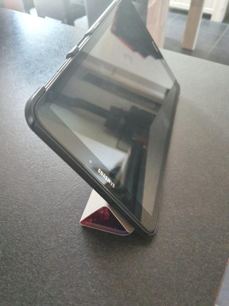 Tablette pos'ee en mode portrait sur une surface fonc'ee, maintenue par sa coque.