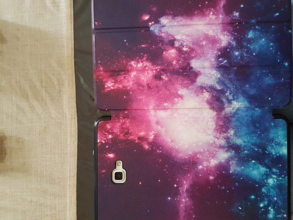 D'etail de la tablette avec sa coque au motif galaxie, l'ecran est 'eteint. On voit le d'ecoupage pour l'appareil photo.