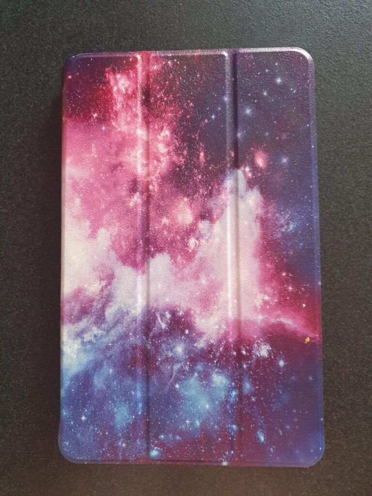 Tablette avec une coque au motif galaxie, ferm'ee, pos'ee sur une surface fonc'ee.