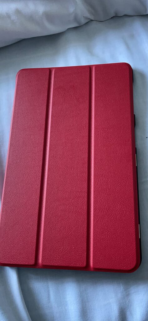 Tablette avec une coque rouge ferm'ee, pos'ee sur un lit.