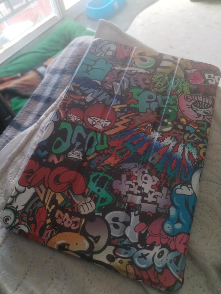 Une tablette ou liseuse avec une coque à motif graffiti, posée sur un coussin ou un lit.