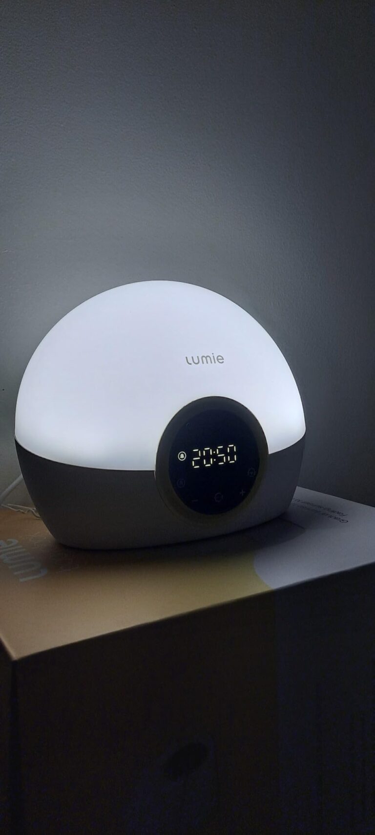 Le réveil Lumie 300 allumé avec une lumière blanche, affichant 20:50, posé sur une table de chevet.