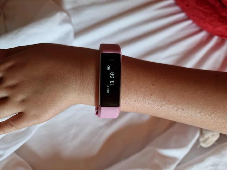 Un bracelet connecté rose à l'écran allumé, sur un poignet
