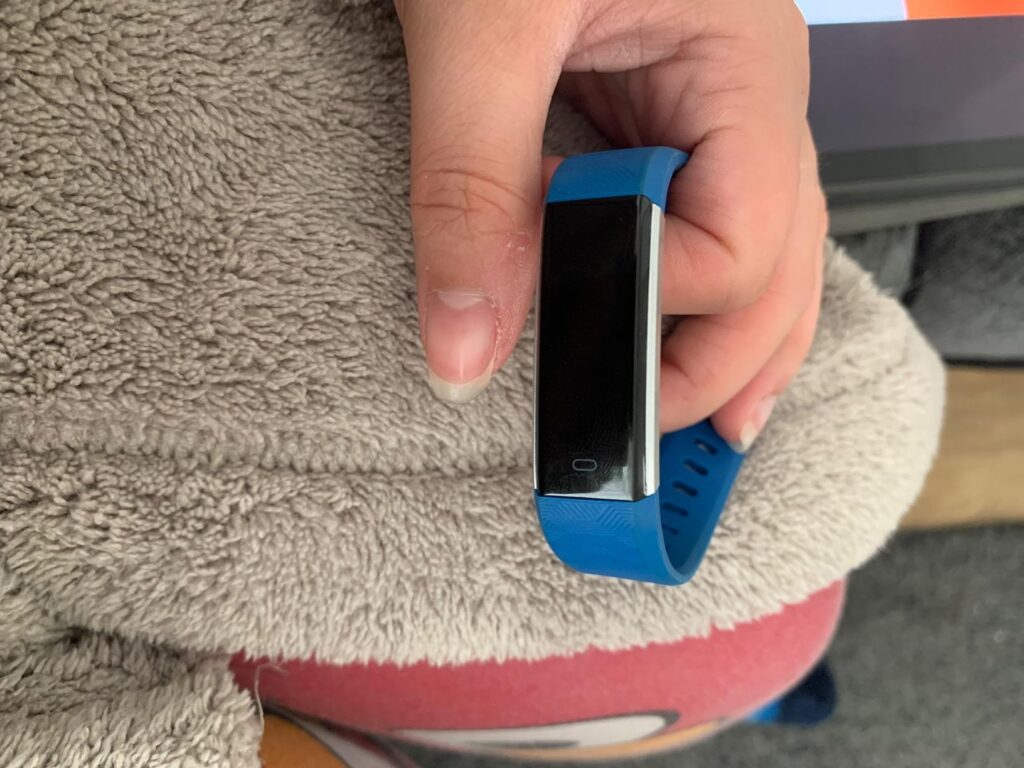 Un bracelet connecté bleu avec l'écran éteint, tenu dans la main