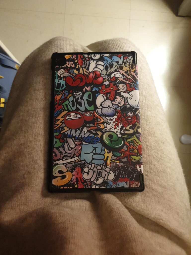 Étui de tablette avec motif graffiti, fermé, posé sur les genoux d'une personne. C'est le même modèle que le visuel 1, sous l...