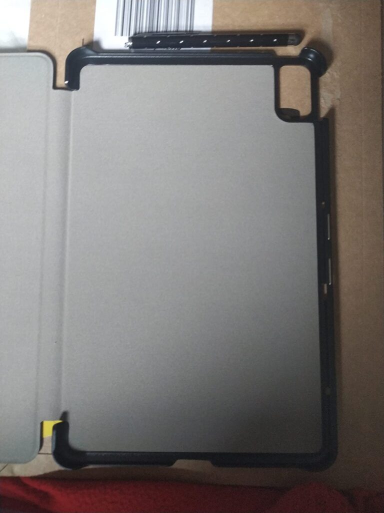 La tablette est présentée dans son étui ouvert, vue de face, posée sur un carton marron. L'étui est ouvert sur la gauche.