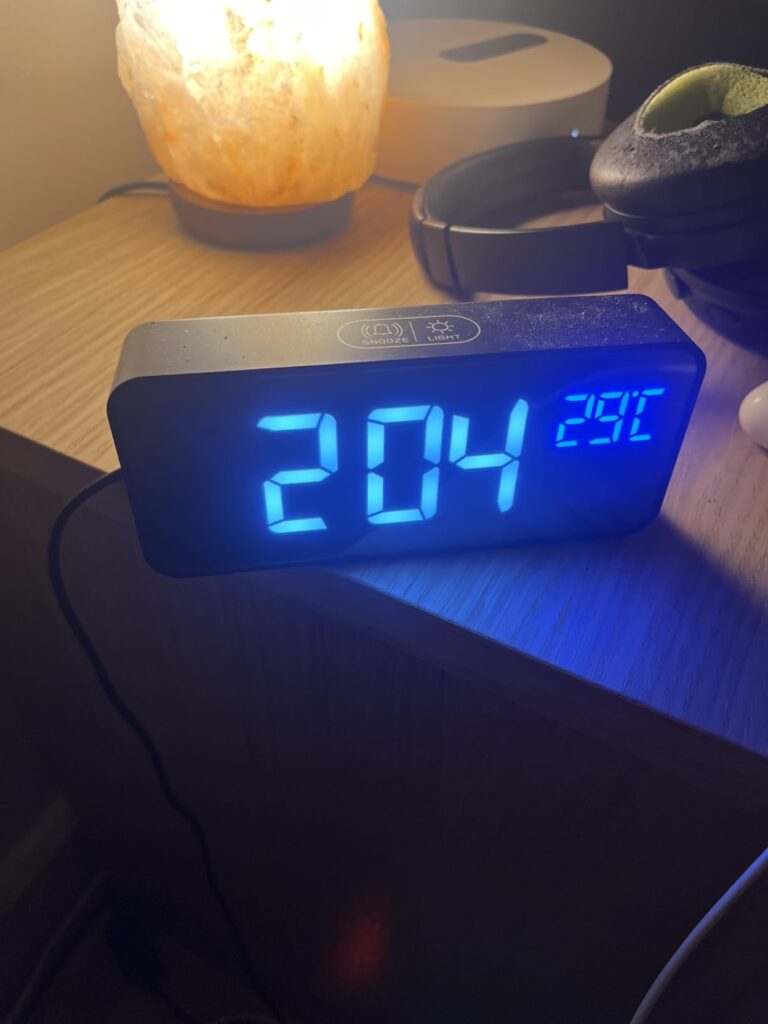 Le réveil sur une table de nuit, avec l'heure 2:04 et la température 29°C affichées en bleu.