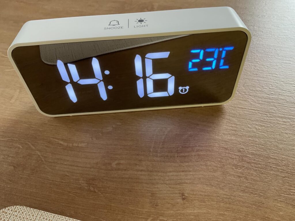 Le réveil blanc sur une surface en bois, affichant l'heure 14:16 et la température 23°C.