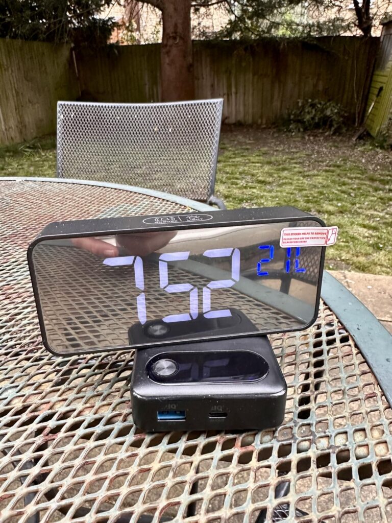Le réveil posé sur une table en métal à l'extérieur, avec un appareil connecté en dessous.