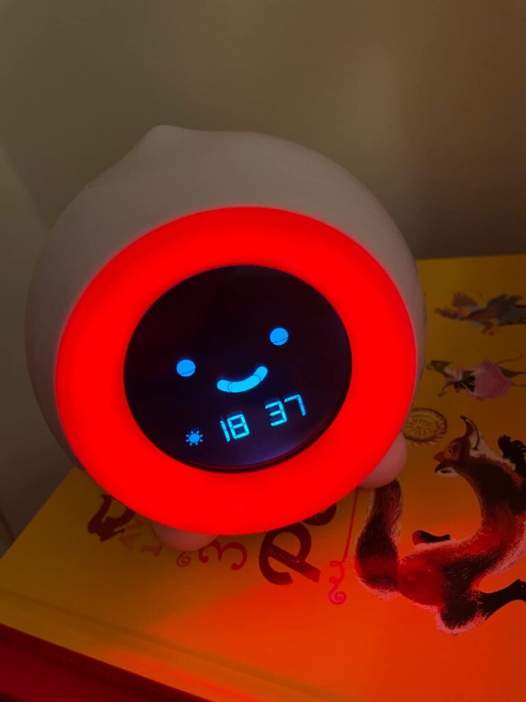 Le réveil posé sur un livre, l'anneau lumineux est rouge et l'heure est 18:37.