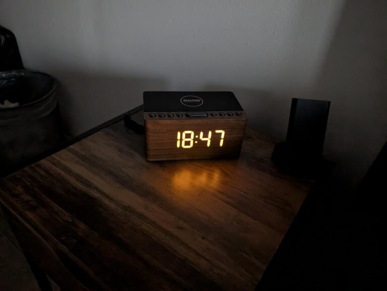 Réveil posé sur une table de chevet, avec l'heure affichée dans le noir.