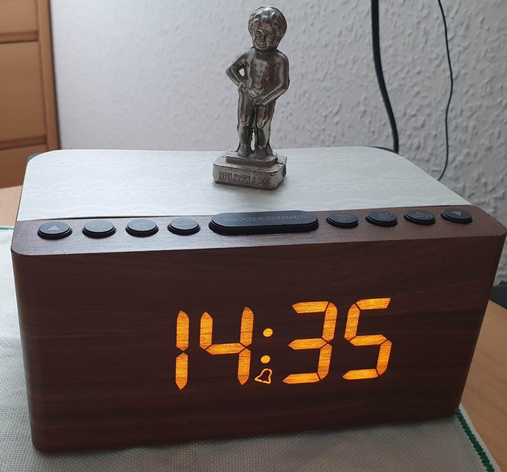Réveil posé sur une commode, avec une statuette dessus et l'heure affichée.