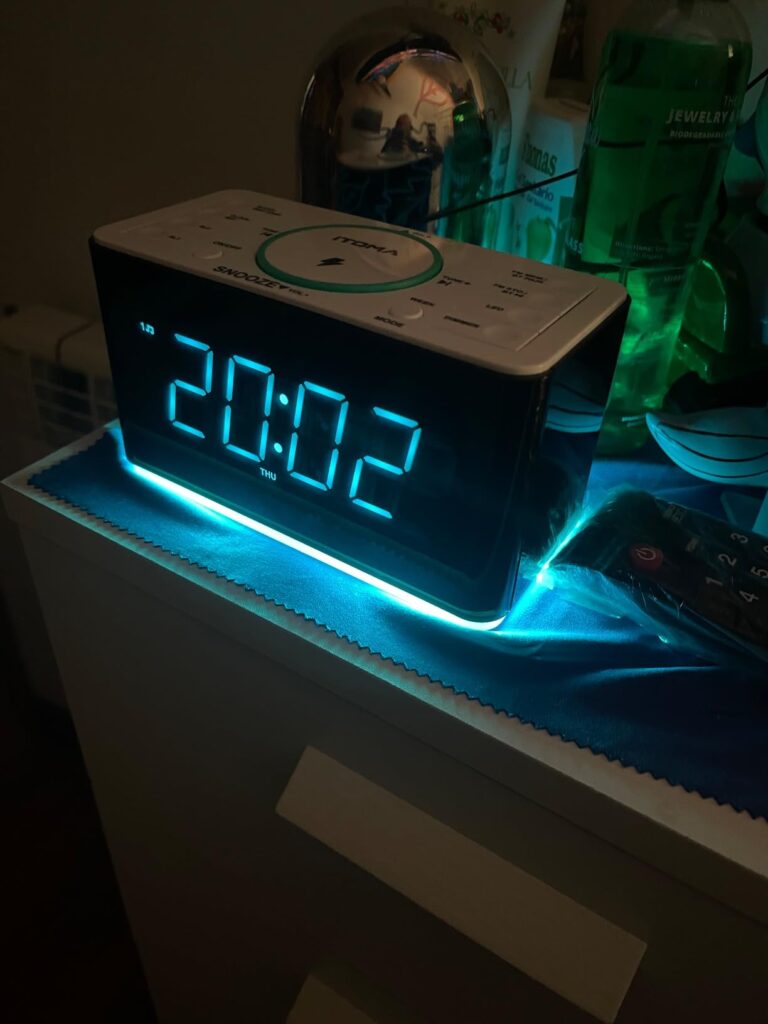 Radio-réveil en situation sur une table de nuit, vue de face. La lumière d'ambiance bleue sous le réveil est allumée. L'affic...