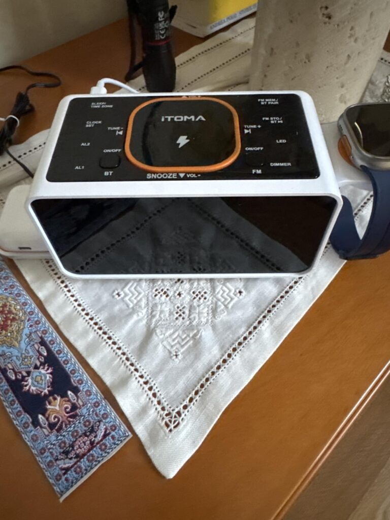 Radio-réveil en situation sur une table de nuit, vue de dessus. Le dessus du réveil est blanc, avec une plaque noire au centr...