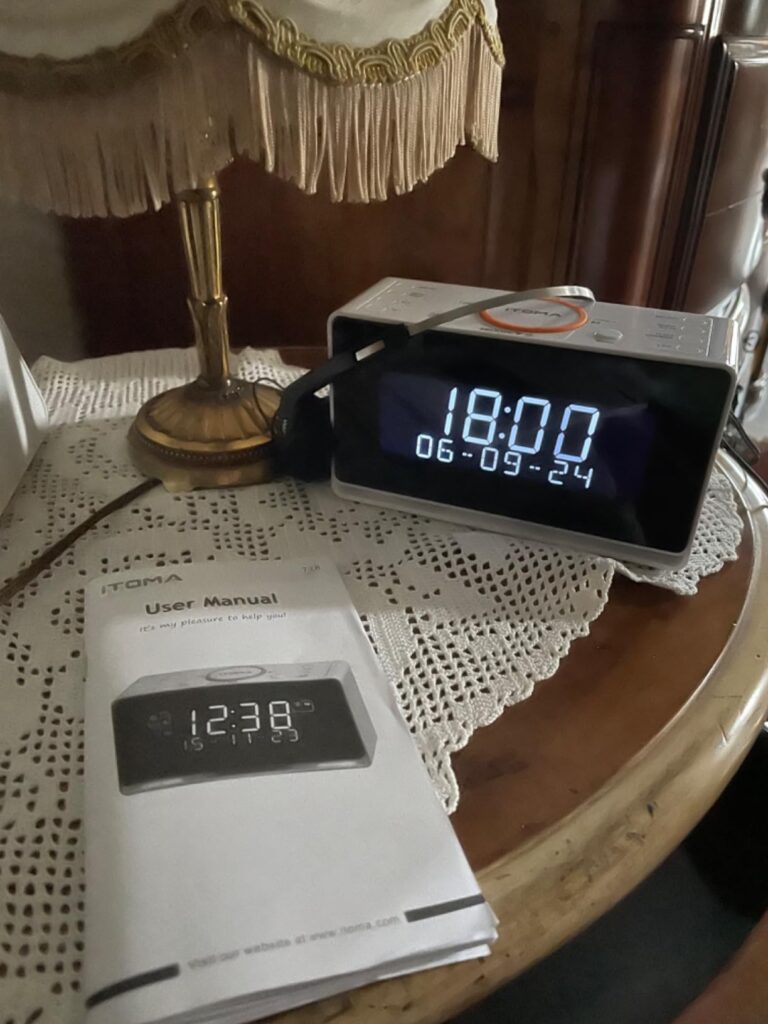 Le réveil radio dans un intérieur, posé sur une table de chevet, avec son manuel d'utilisation à côté.