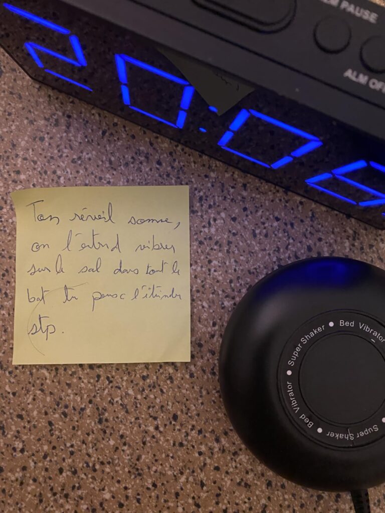 Réveil et vibreur sur une table, avec un post-it manuscrit. L'heure affichée est 20:06.
