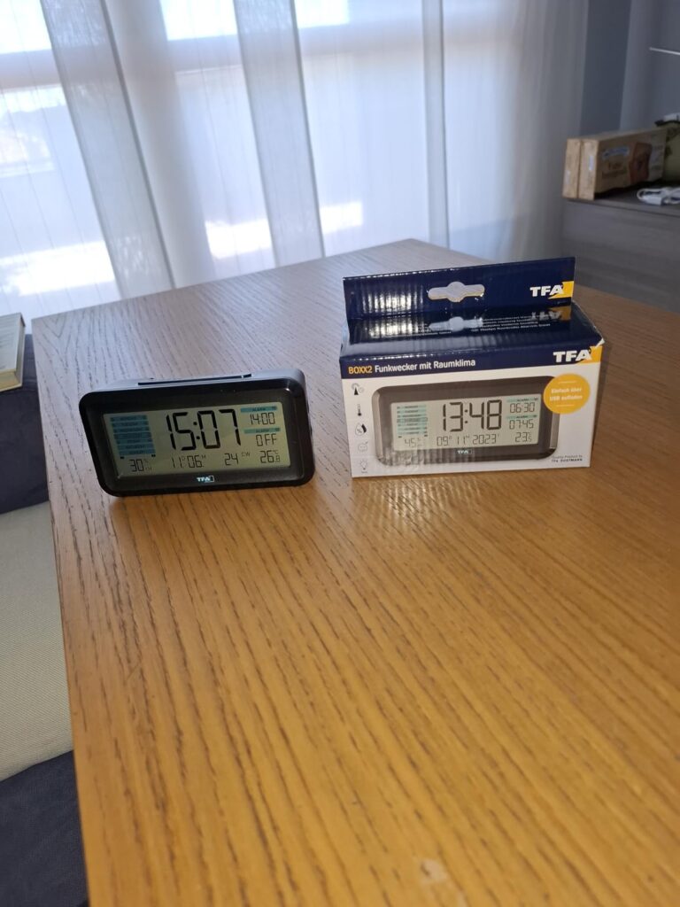 Le réveil sur une table à côté de son emballage, montrant le produit hors de sa boîte et la boîte.