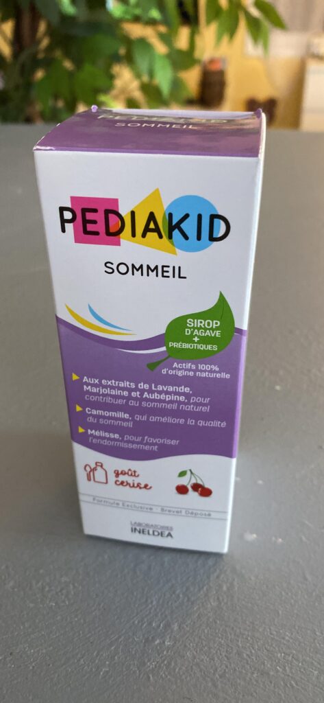 Boîte de sirop Pediakid Sommeil, vue de côté, dans un environnement avec des plantes floues en arrière-plan.