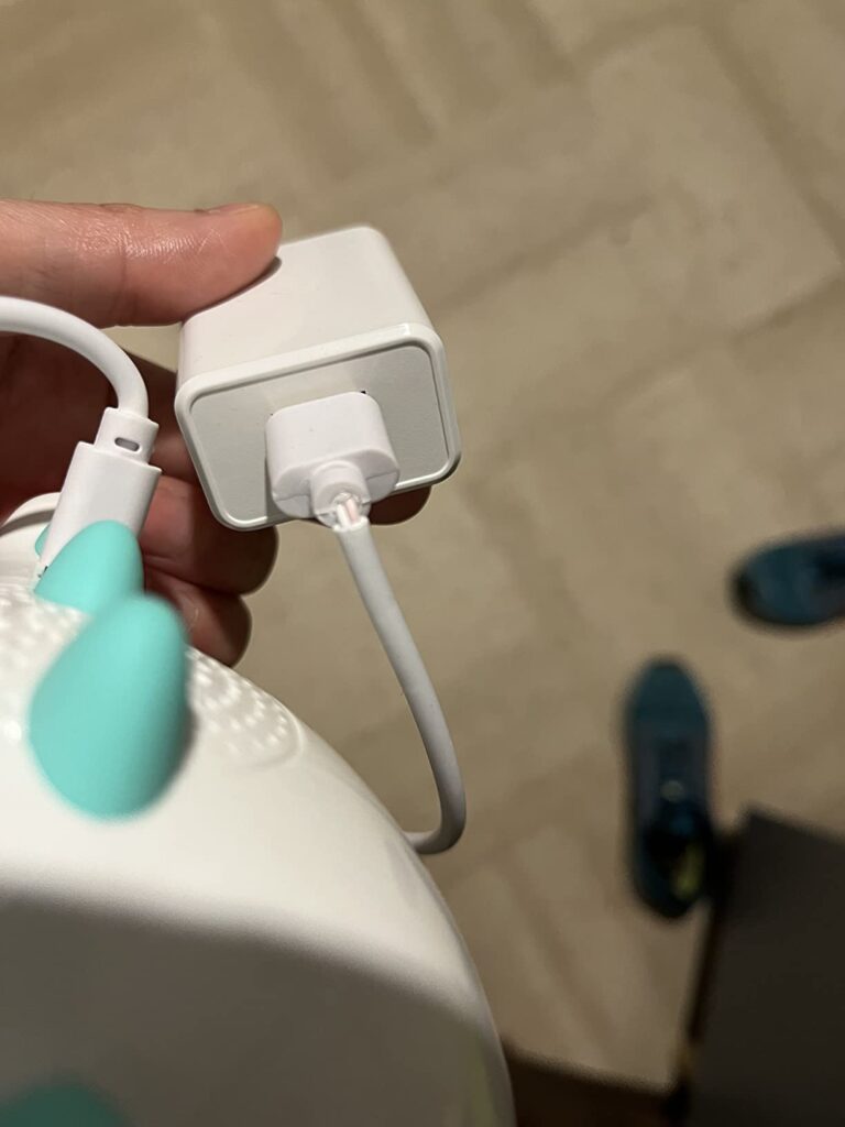 Un gros plan sur le connecteur de charge du réveil, branché à un adaptateur secteur. La main de la personne tient l'adaptateu...