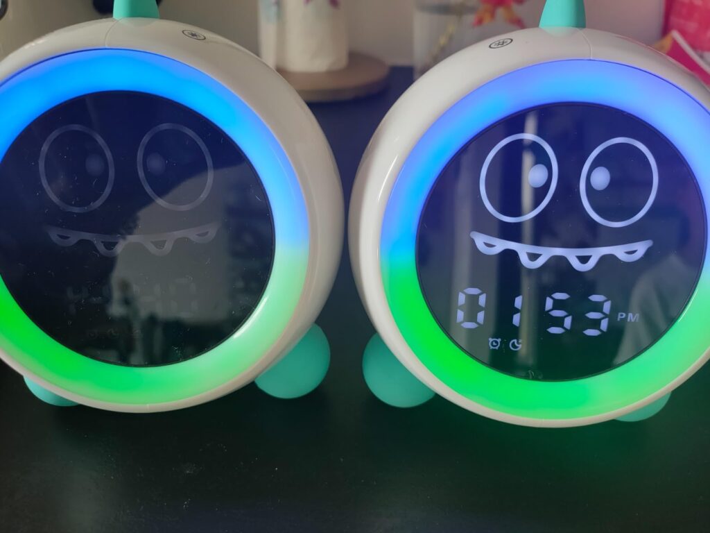 Deux réveils identiques, un éteint et un allumé, affichant l'heure 01:53 avec une expression de monstre joyeux et une animati...