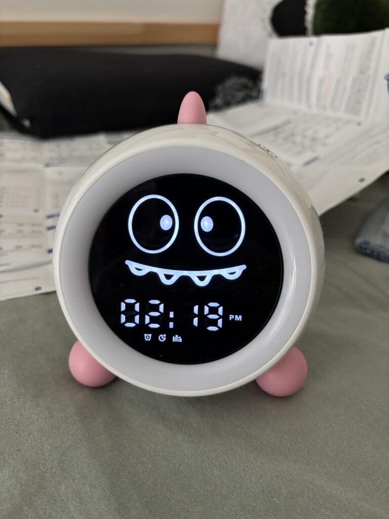 Le réveil est posé sur une table et affiche l'heure 02:19 avec une expression de monstre joyeux et une animation de clignotem...