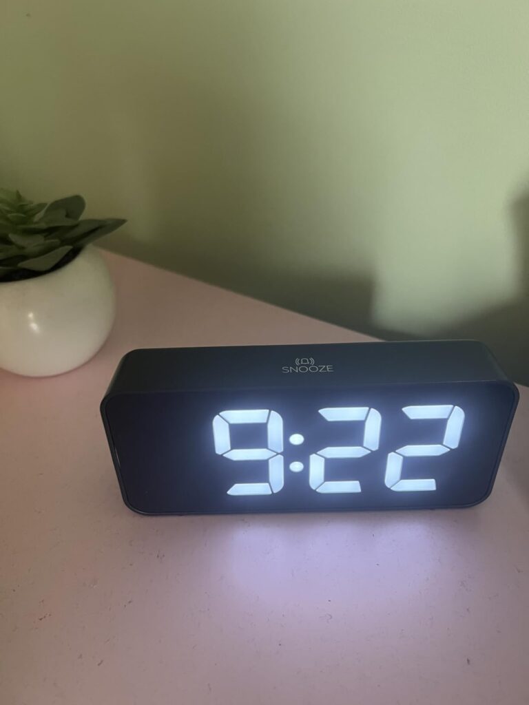 Le réveil sur une table de chevet, l'heure en blanc et très lumineuse. Plante en arrière plan.