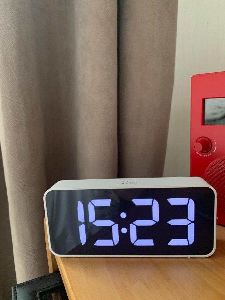 Le réveil sur une table de chevet, l'heure en bleu clair. Rideau et radio en arrière plan.