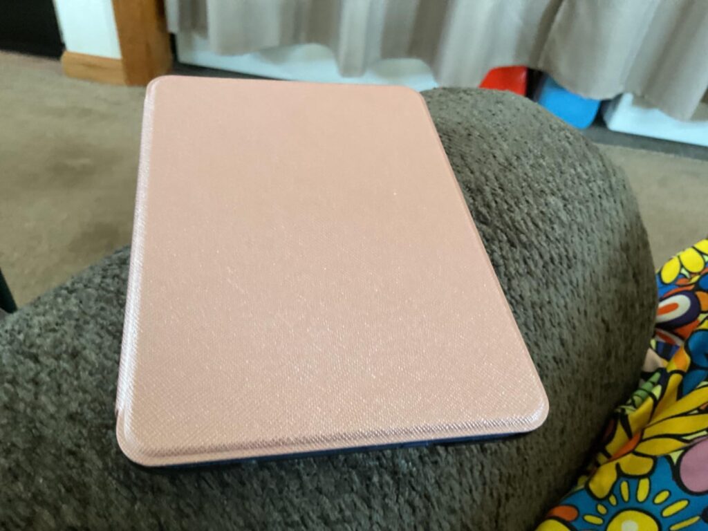 Liseuse avec une coque rose posée sur un canapé, vue de dessus. C'est la même coque que le visuel 2, sous un angle différent.