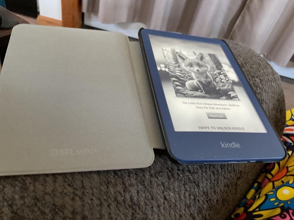 Liseuse Kindle bleue ouverte avec son étui gris-beige, posée sur un canapé. L'écran affiche un renard.