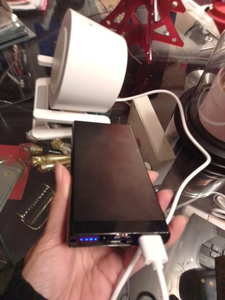 Le produit est branché à une batterie externe. La batterie externe est dans la main d'une personne.