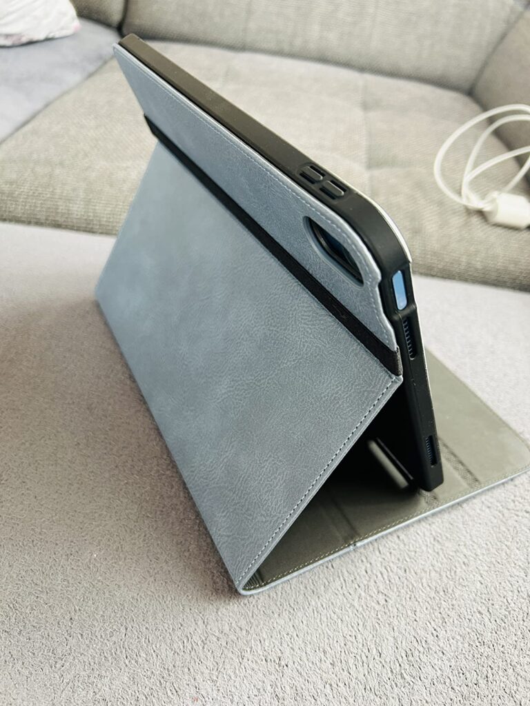 Une tablette équipée de la coque est posée sur un canapé, en mode chevalet, sous un autre angle. L'élastique de fermeture est...