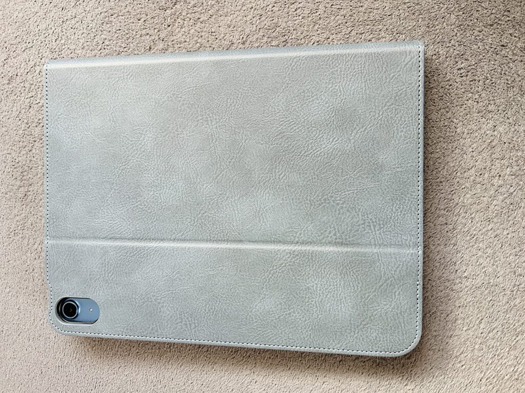 Vue de dessus d'une coque pour tablette en simili-cuir gris clair, de dos. Le logement de l'appareil photo est visible en bas...