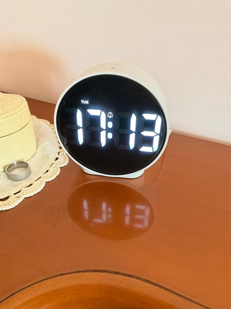 Le réveil sur une table de chevet, l'heure affichée est 17h13, avec un reflet sur la surface.