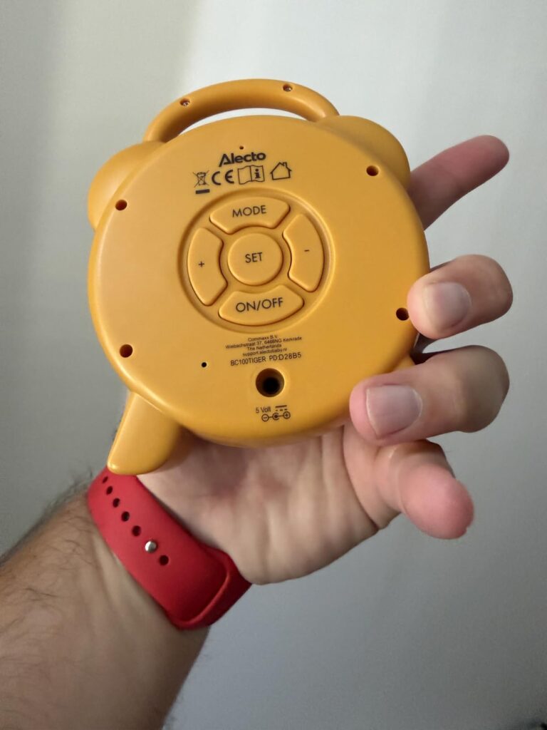 L'arrière du réveil jaune dans une main, montrant les boutons et les informations de certification.