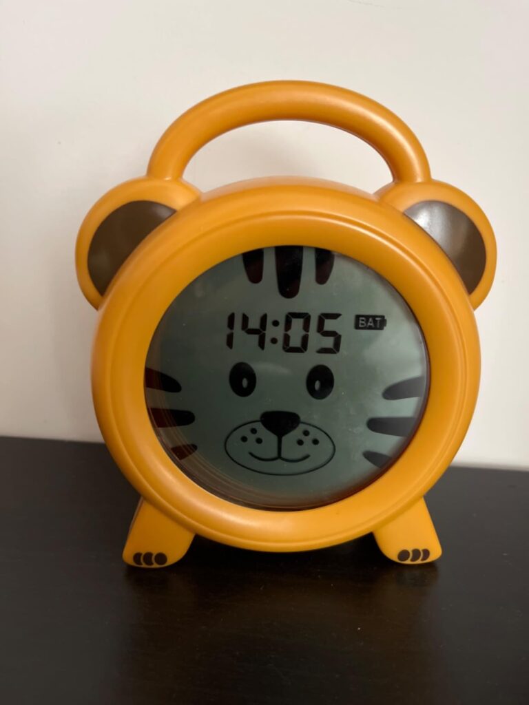 Le réveil jaune en forme de tête de tigre affichant 14h05, posé sur une surface sombre.